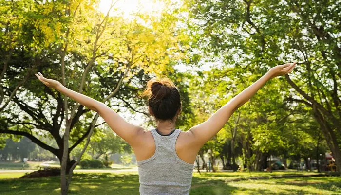 A shot composed of a woman outdoors outstretching her arms with sunlight coming through the trees